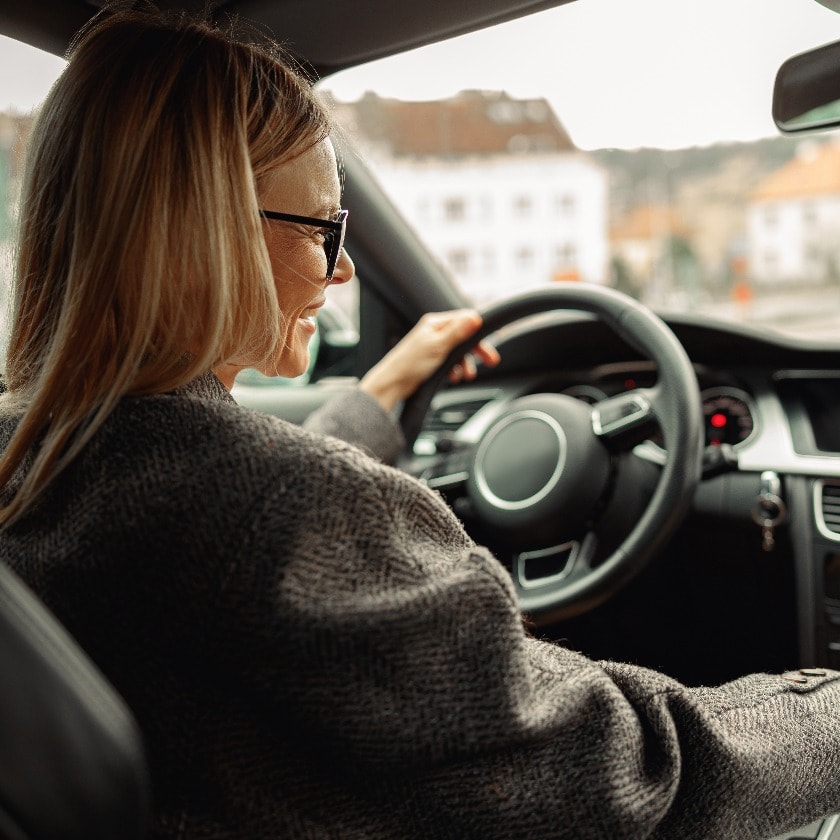 Attractive woman driving car in city with one hand on steering wheel and another on gear lever