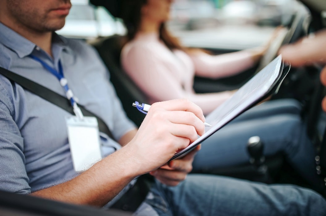 Male auto instructor takes exam in young woman. Close up of man writing on paper. Passing practical test. Young woman driving with confidence.