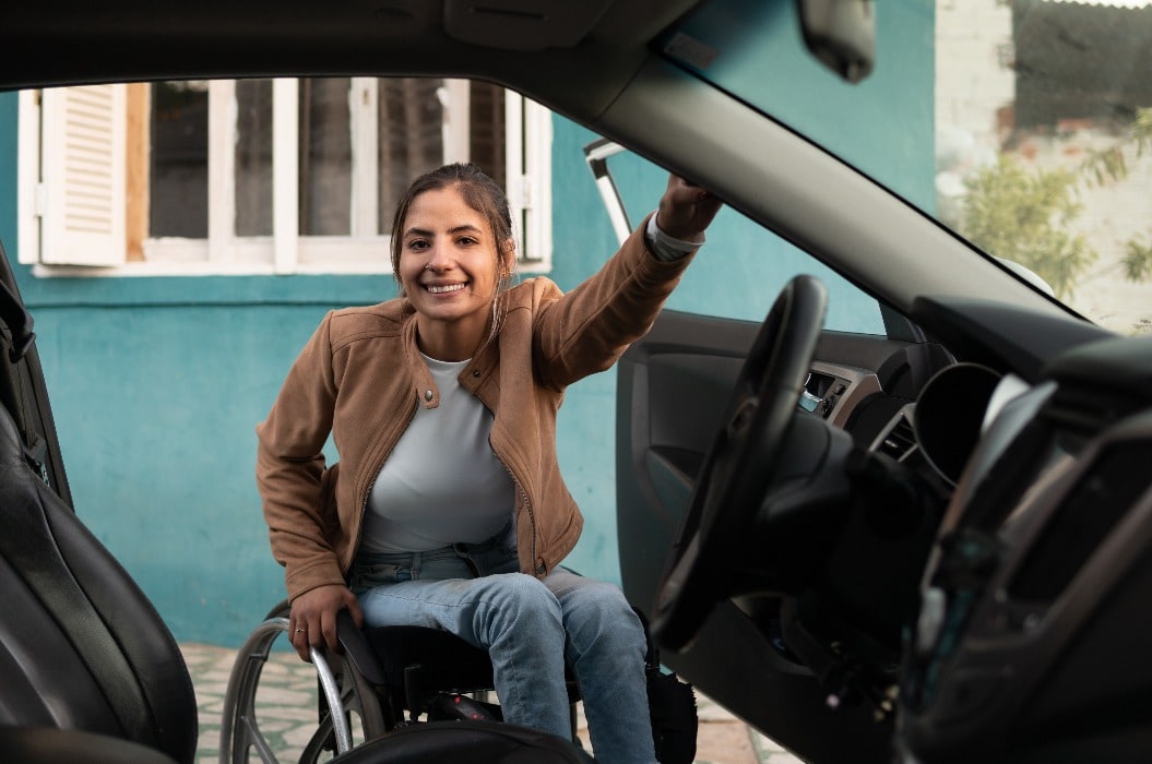 wheelchair woman in front of car and looking at camera.