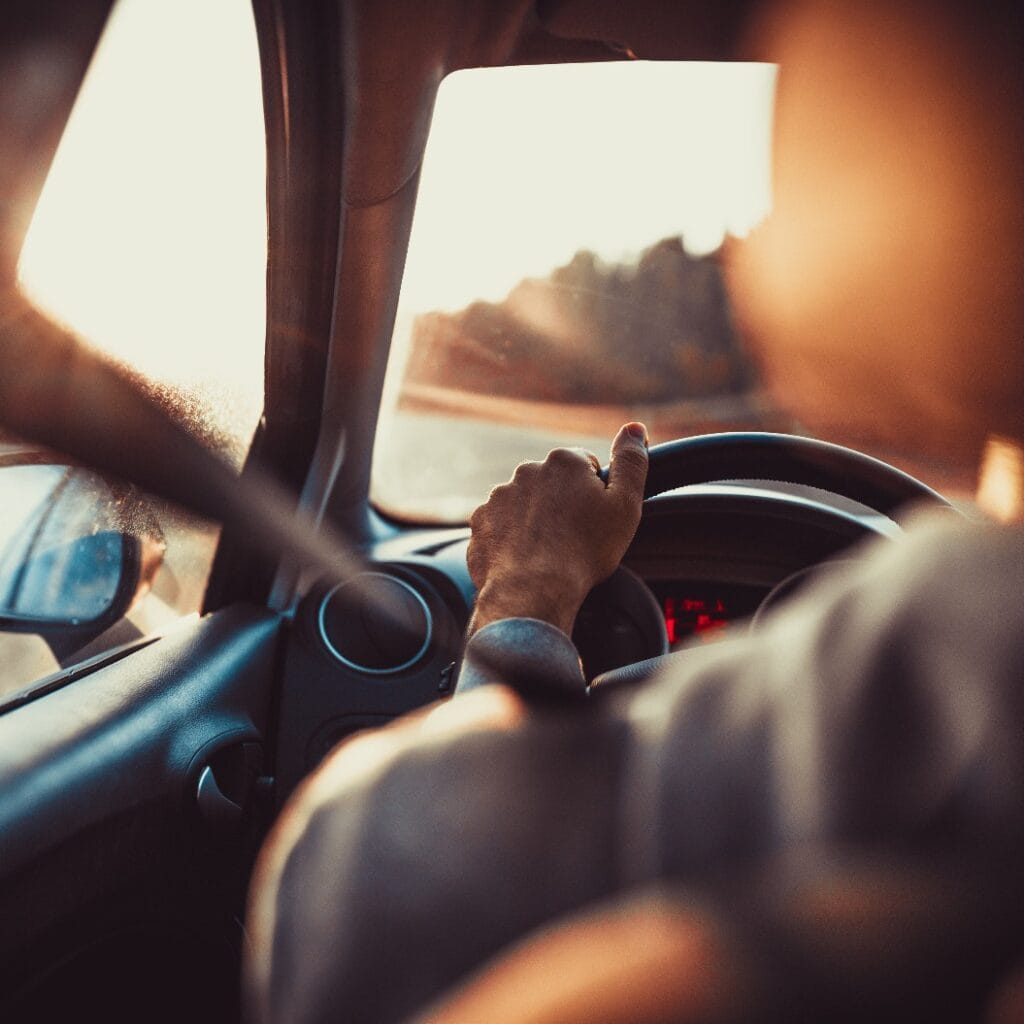 Man driving car, hand on steering wheel, looking at the road ahead,sunset.